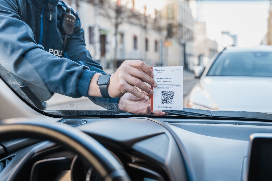 Bussenzettel mit QR-Code wird von einem Polizisten unter dem Scheibenwischer angebracht.